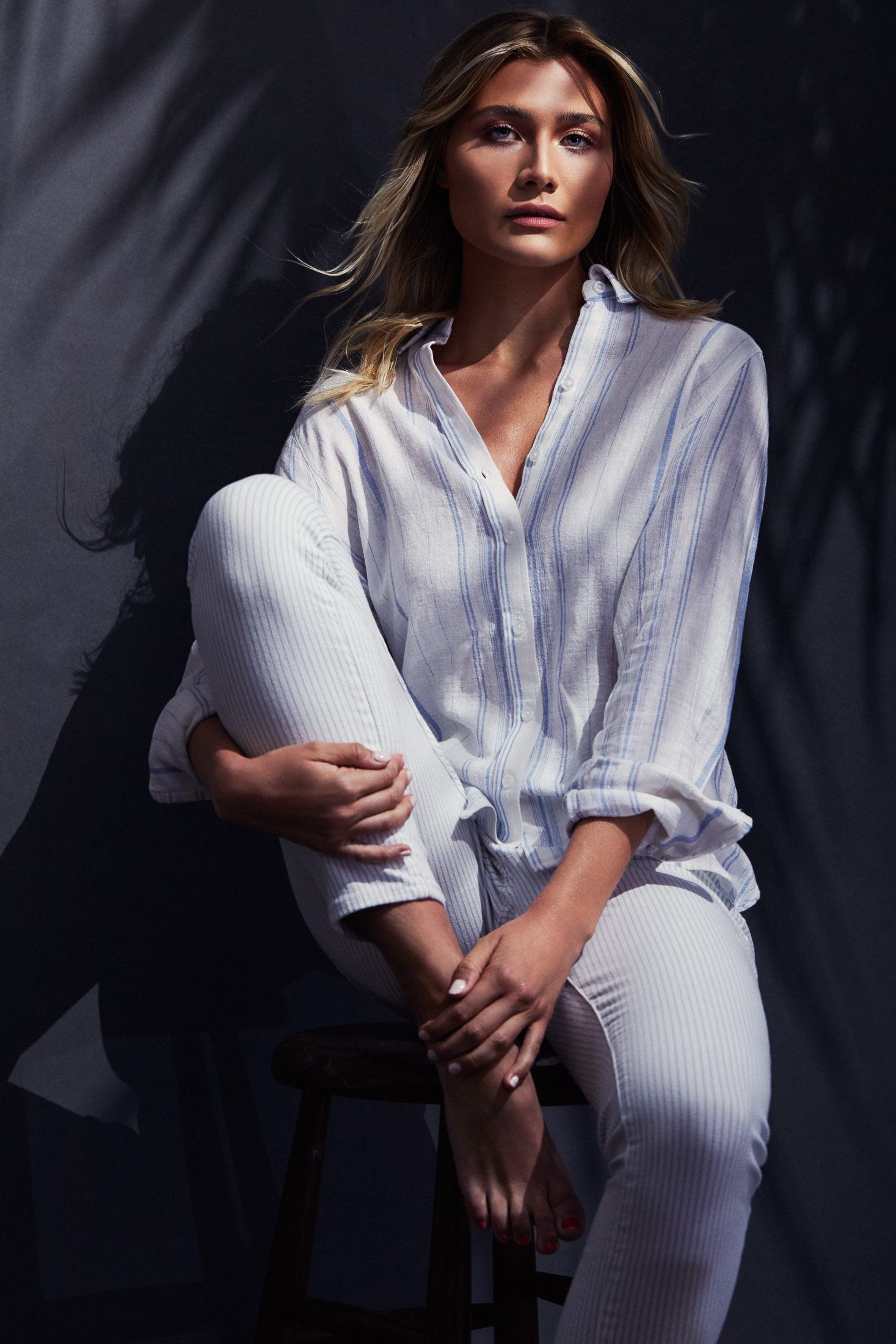 Seated editorial portrait with palm leaf shadows