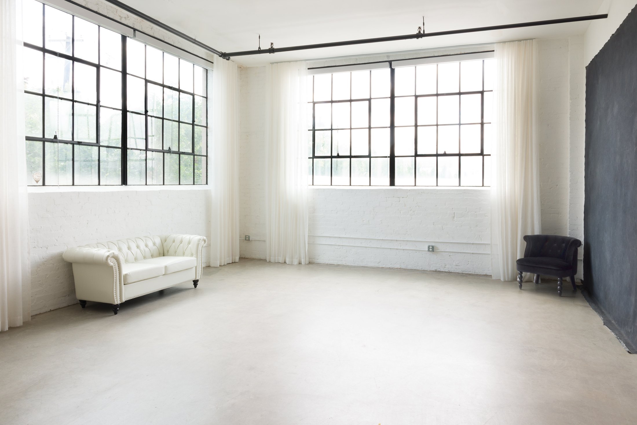 The AJK Images portrait studio in Fair Park, Dallas: white brick, steel-frame windows, sheer drapes, and a hand-painted canvas backdrop