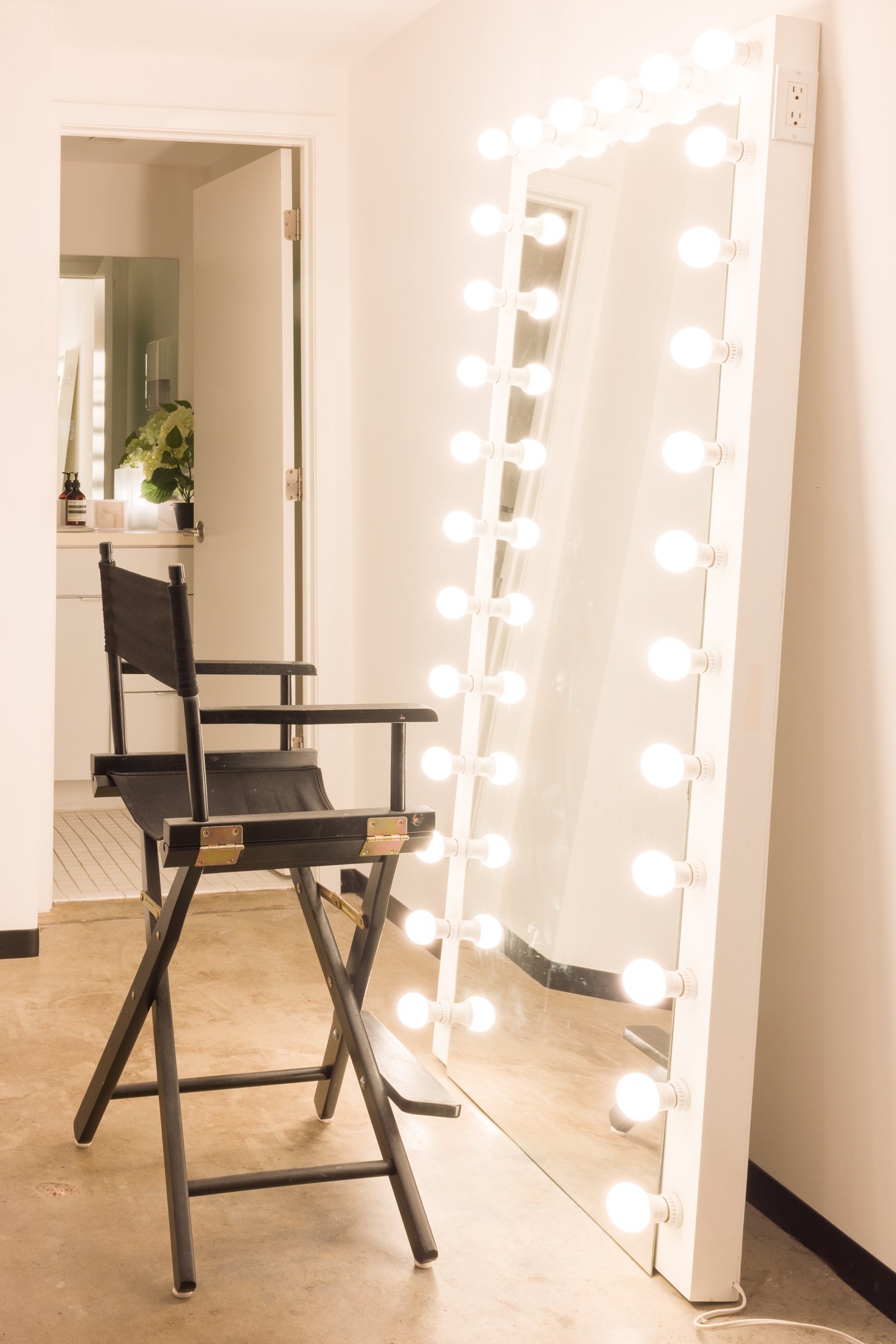 Hair and makeup station with a lit vanity mirror and director&rsquo;s chair at the AJK Images studio