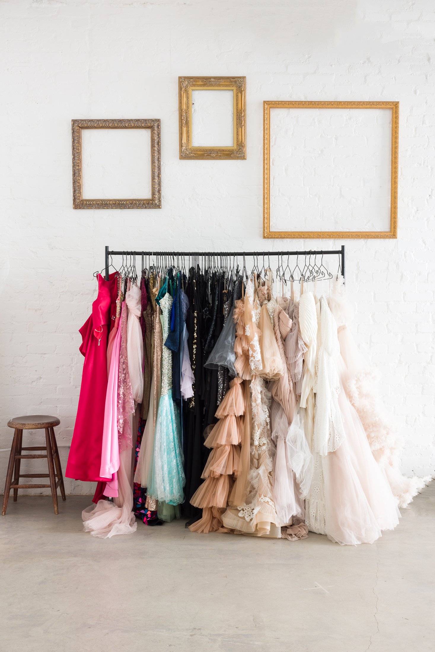 Gowns and textiles on the wardrobe rack beneath vintage gold frames at the AJK Images studio